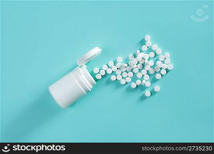 bottle with white pills coming out over green background medical concept