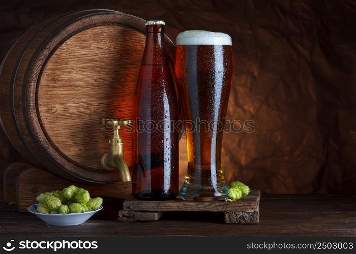Bottled and unbottled beer glass with barrel and fresh hops for brewing still-life