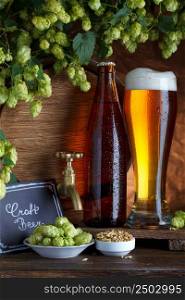 Bottled and unbottled beer with barrel, barley and fresh hops for brewing still-life