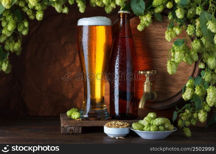 Bottled and unbottled beer with barrel, barley and fresh hops for brewing still-life