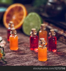 Bottles filled with red and orange essential oils. Fresh citrus fruit, orange and lime cut in half. Aromatherapy relax concept.