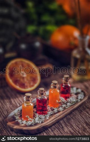 Bottles filled with red and orange essential oils on wooden board. Fresh citrus fruit cut in half. Aromatherapy relax concept