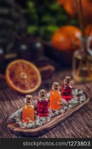 Bottles filled with red and orange essential oils on wooden board. Fresh citrus fruit cut in half. Aromatherapy relax concept