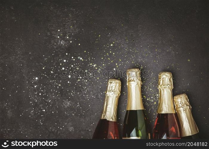 Bottles of champagne with gold glitter and space for text on dark background, top view. Hilarious celebration. Bottles of champagne with gold glitter and space for text on dark background