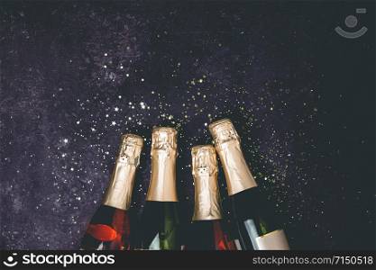 Bottles of champagne with gold glitter and space for text on dark background, top view. Hilarious celebration