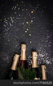 Bottles of champagne with gold glitter and space for text on dark background, top view. Hilarious celebration