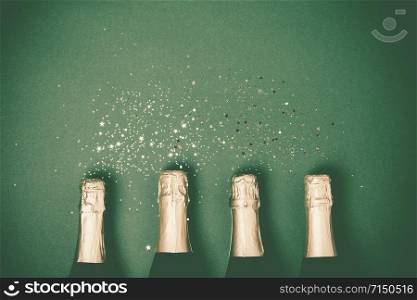Bottles of champagne with gold glitter and space for text on green background, top view. Hilarious celebration