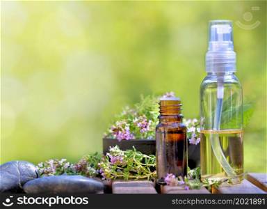 bottles of essential oil and flowers of aromatic herb on a table and on green background