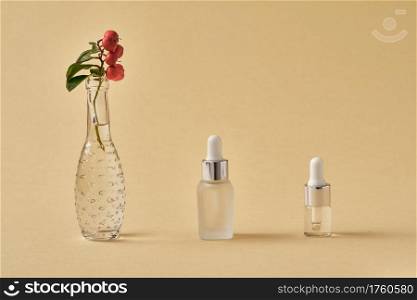 Bottles of essential oil with fresh wintergreen plant in a vase on beige background