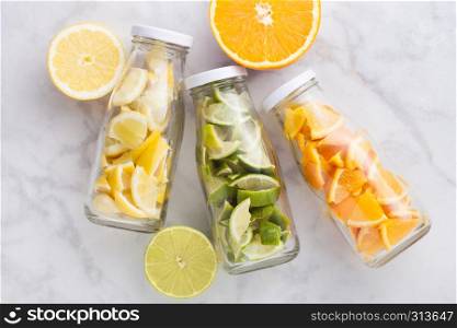 Bottles of fresh summer water with oranges with limes and lemons slices on marble background with fresh fruits