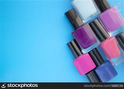 Bottles of nail polish. A group of bright manicures on a blue background. With empty space on the left. View from above. Bottles of nail polish. A group of bright manicures on a blue background. With empty space on the left.