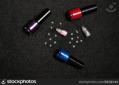 Bottles of nail polish with nail decorations displayed on a black background