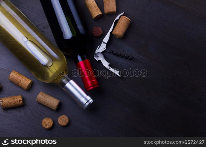 Bottles of red and white wine with corks on wooden table. Glass of red wine