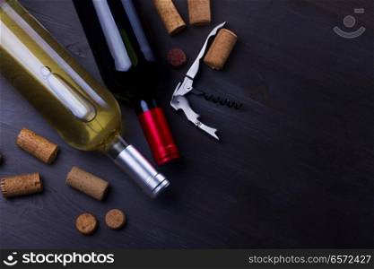 Bottles of red and white wine with corks on wooden table. Glass of red wine