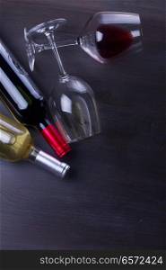 Bottles of red and white wine with glasses on wooden table. Glass of red wine