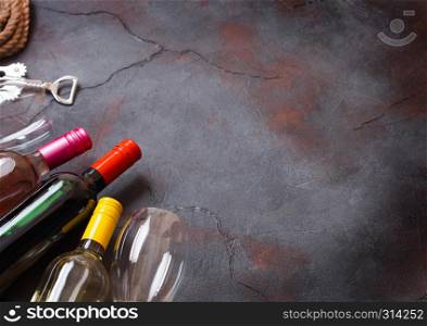 Bottles of red white and pink rose wine with glasses and corkscrew opener on stone kitchen table background. Top view
