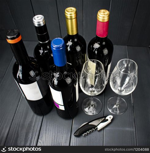 Bottles of red wine from different manufacturers with two sparkling wine glasses and a corkscrew for tasting, in well-lit gray wooden space