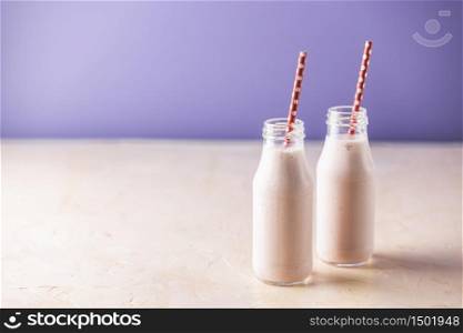 Bottles with delicious strawberry milkshake or smoothie on table and violet background.
