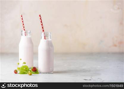 Bottles with delicious strawberry milkshake or smoothie with branch of wild strawberry on table and pink background.