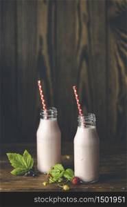 Bottles with delicious strawberry milkshake or smoothie with branch of wild strawberry on dark wooden table and background.