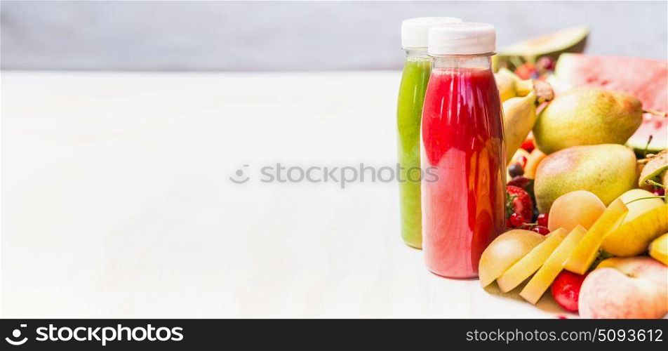 Bottles with red and green smoothies and juices beverages on white table background with summer fruits and berries, front view, banner. Healthy food and vegetarian eating concept