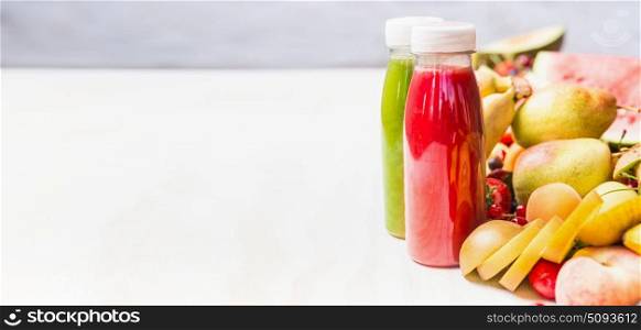 Bottles with red and green smoothies and juices beverages on white table background with summer fruits and berries, front view, banner. Healthy food and vegetarian eating concept