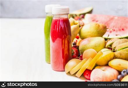 Bottles with red smoothies and juices beverages on white table background with summer fruits and berries, front view. Healthy food and vegetarian eating concept