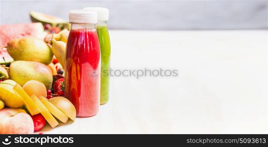 Bottles with smoothies and juices beverages on white table background with summer fruits and berries, front view, banner. Healthy food and vegetarian eating concept