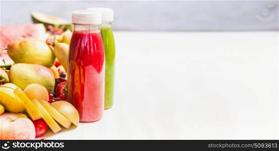 Bottles with smoothies and juices beverages on white table background with summer fruits and berries, front view, banner. Healthy food and vegetarian eating concept