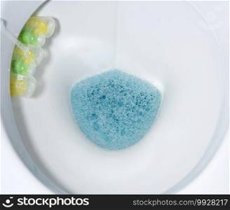bottom of white toilet bowl with blue water and solid disinfectants, top view