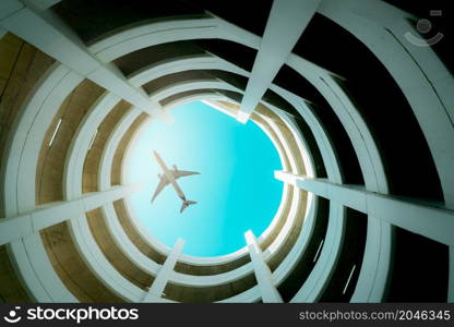 Bottom view multi-story car park building with plane flying above building. Air logistic. Aviation and travel business. Architecture of spiral curve building. Airline business. Tourism transportation