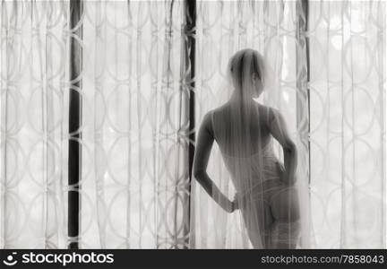 Boudoir, attractive young woman wearing lingerie and she stands front of the window - black and white image