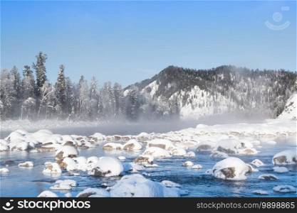 Boulders in cold water are covered with snow. Winter river on frosty morning.