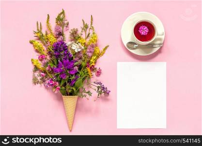 Bouquet colored wildflowers flowers in ice cream waffle cone, cup of tea and blank empty paper card for text on pink background Creative Top view Flat Lay Mock up Template for postcard or your design.. Bouquet colored wildflowers flowers in ice cream waffle cone, cup of tea and blank empty paper card for text on pink background Creative Top view Flat Lay Mock up Template for postcard or your design