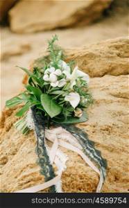 bouquet of a bride from feces and roses lies on a sandstone stone on the seashore