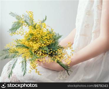Bouquet of bright, yellow flowers in the hands of a young woman in a white dress. Isolated, close-up. Wedding preparations. Bouquet of bright, yellow flowers. Wedding preparations
