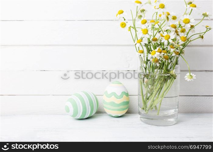 Bouquet of chamomiles in a glass vase and easter eggs in pastel color on white wooden table. Bouquet of chamomiles in a glass vase and easter eggs in pastel color on white wooden table.