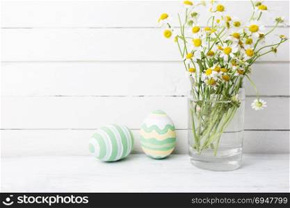 Bouquet of chamomiles in a glass vase and easter eggs in pastel color on white wooden table. Bouquet of chamomiles in a glass vase and easter eggs in pastel color on white wooden table.