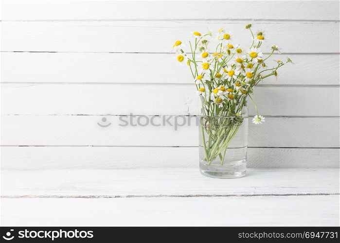 Bouquet of chamomiles in a glass vase on wooden background