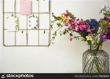 Bouquet of colorful flowers white wall and post cards hanging, modern interior retro. Bouquet of colorful flowers white wall and post cards hanging, modern interior