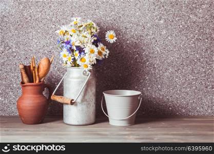 Bouquet of daisies in a vintage tin can, bucket and rough ceramic jug with wooden cooking utensil set. The rustic decor