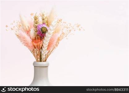 bouquet of dried flowers and spikelets in neck of ceramic bottle on light pink background with copyspace