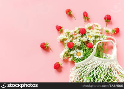 Bouquet of field daisies in reusable shopping eco mesh bag and red strawberries on pink background. Concept no plastic and zero waste. Copy space Top view .. Bouquet of field daisies in reusable shopping eco mesh bag and red strawberries on pink background. Concept no plastic and zero waste. Copy space Top view