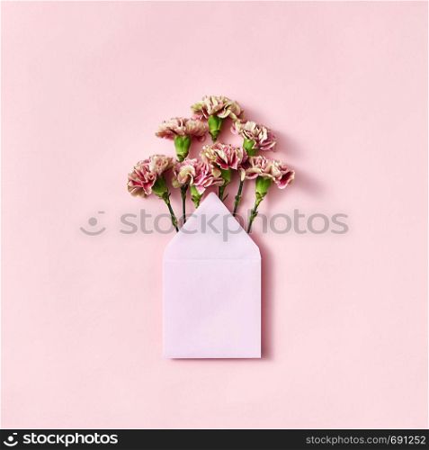 Bouquet of fresh carnations in a handmade blank envelope on a light pink background with copy space. Mock-up. Top view.. Mock up envelope with pink carnations for congratulation on a pastel pink background.