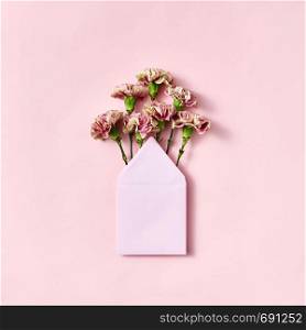Bouquet of fresh carnations in a handmade blank envelope on a light pink background with copy space. Mock-up. Top view.. Mock up envelope with pink carnations for congratulation on a pastel pink background.