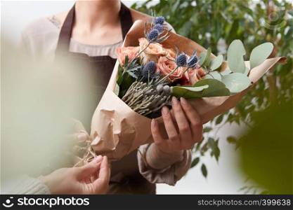 Bouquet of fresh fragrant roses living coral color in a paper with blured green leaf background. Concept of Mother Day.. Close-up of roses flowers bouquet in a woman's hands on a blured green leaf background.