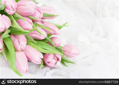 Bouquet of fresh pink tulips flowers covered with dew drops are on lacy textile close-up