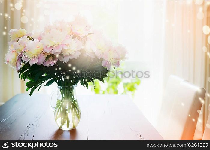 Bouquet of peonies in glass vase on a table against the window, indoor. Home decoration.