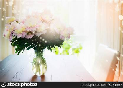 Bouquet of peonies in glass vase on a table against the window, indoor. Home decoration.