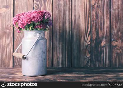 Bouquet of pink carnations in a vintage tin can on wooden background. Rustic decorative setting